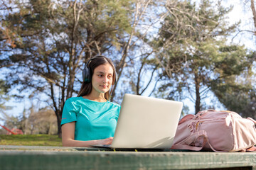 Female university student studying, using a laptop and sitting outside in a park
