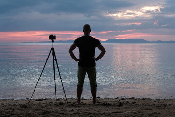 A tourist (photographer) takes a sunset on a camera mounted on a tripod on the beach. Klong Muang...