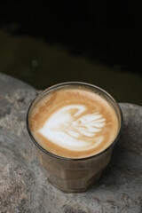Art coffee latte on the small glass beside a fish pool