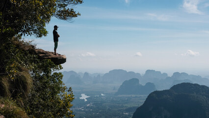 A tourist stands on the rock overhanging a abyss on sunny day.  Dragon's Crest (Khao Ngon Nak)...