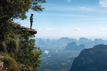 A hiker stands on the rock overhanging a abyss on sunny day. Dragon's Crest (Khao Ngon Nak) Viewpoint, Thailand.