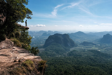 Fototapeta na wymiar A tourist stands on the rock overhanging the plain on sunny day. Dragon's Crest (Khao Ngon Nak) Viewpoint, Krabi Province, Thailand.