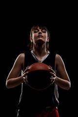 Fototapeta na wymiar Female basketball player. Beautiful girl holding ball. Side lit half silhouette studio portrait against black background.