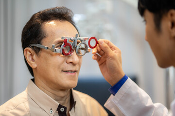 Portrait of young ophthalmologist putting trial frame on male patient during vision check in modern...