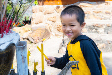 Young Asian children learning  Excited and fun with activities to pay homage to the Buddha image in the temple by lighting candles to pay respect to sacred things.