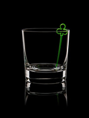 A glass whiskey glass with a green skewer inside in the form of clubs on a black background. Silhouette. Casino. Card games. Luck. Symbol. Art. Design.
