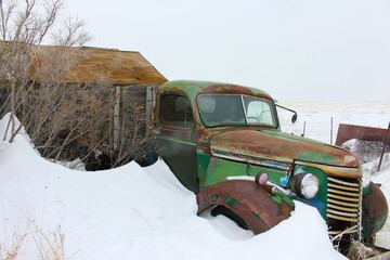 rusted farm truck buried in the snow on the prairie