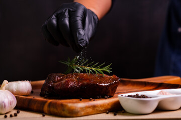 professional Chef hands cooking meat steak and adding salt on black copy space background for menu restaurant or recipe text.