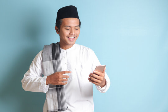 Portrait of young Asian muslim man holding mobile phone with smiling expression on face. Isolated image on white background