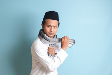 Portrait of Asian muslim man in white koko shirt doing martial arts gesture or pencak silat. Isolated image on blue background