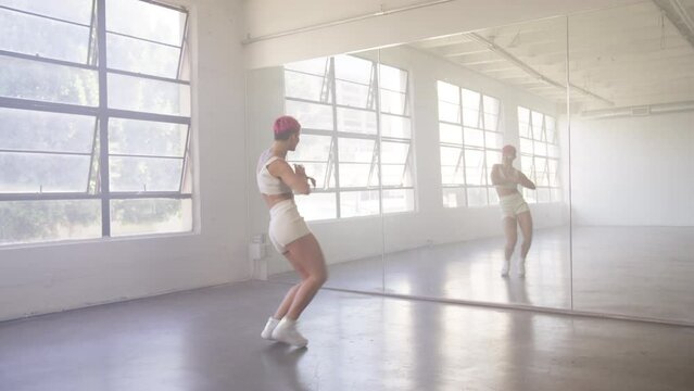 Young beautiful girl with pink hair moving body enjoying practice looking at mirror reflection. People and leisure activities concept 4K. Alone dancer woman dancing hip-hop in urban dancehall indoors