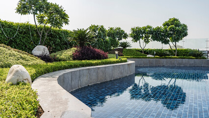 The swimming pool is surrounded by a curly barrier and an ornamental garden. Boulders in the green...
