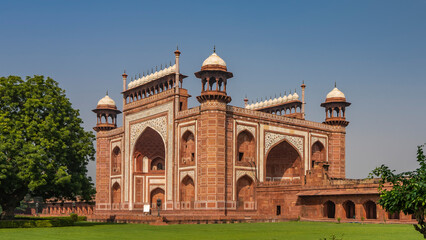 Fototapeta na wymiar The ancient mosque Kau Ban in the Taj Mahal complex is built of red sandstone and white marble. Arches, towers, domes, inlays of precious stones are visible. Green vegetation around. Blue sky. India