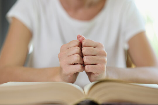 Woman sits at table with thick open book and holds her fists on book pages.