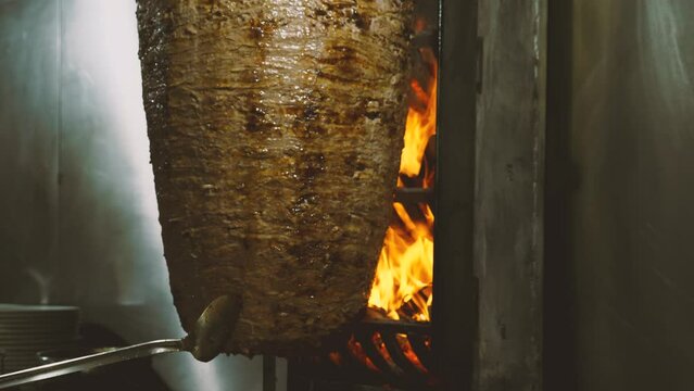 A rotisserie with meat for shawarma, doner kebab, or horos spins next to a fire. Close-up. Slow-motion footage. Lamb meat assembled on a vertical skewer and grilled over the coals. Turkish Cuisine