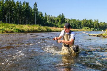 Mann geht seinem Hobby-Sport Fliegenfischen in idyllischer Landschaft an einem kleinen Fluss nach