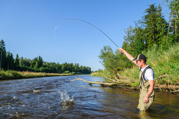 Angler beim Fliegenfischen in sommerlicher Landschaft