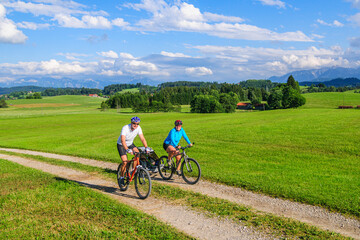 Eltern mit Nachwuchs im Buggy unterwegs mit dem Mountainbike, die Voralpen-Landschaft im Allgäu...