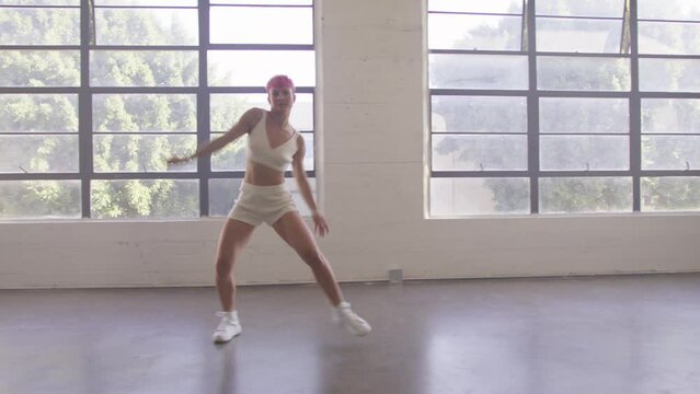 Happy beautiful caucasian woman walking and dancing indoor. Young carefree girl with short pink hair enjoys day and dancing in urban dance studio. Funky lady performing dance walk dolly shot 4K RED