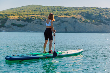 Young woman on stand up paddle board at quiet sea with beautiful landscape.
