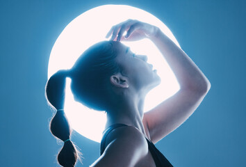 Fototapeta premium Beauty, light and profile of a model in a studio with a sensual, soft and attractive pose. Cosmetic, magical and slim woman with a mystical glow posing by a moon while isolated by a blue background.