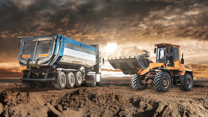 Fototapeta premium A loader or bedozer loads a dump truck car with sand at a construction site. Loading a vehicle for transporting soil. A loader or bulldozer moves the soil. equipment for earthworks.