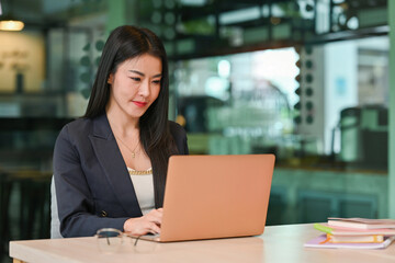 Positive focused Mature Business lady working with laptop at table in Co working space.