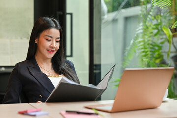 Portrait of a businesswoman working at office reading paper report in file folder.