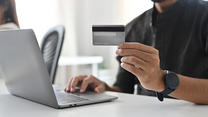 Close up and cropped of Young Asian Businessman holding credit card and using laptop.