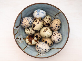 top view of many boiled quail eggs in ceramic bowl on light brown wooden table