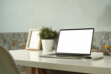 Comfortable workplace with laptop computer, smart phone, picture frame and potted plant in white table