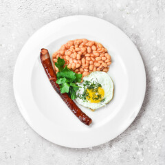 Breakfast. Eggs with sausage and beans. On a white plate. On a gray stone background. Restaurant menu.