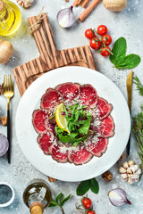 Veal carpaccio with lemon and arugula. On a white plate. On a gray stone background. Restaurant menu.