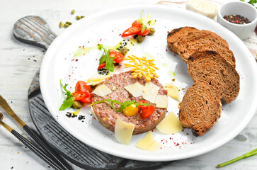 Veal tar-tar, with toast bread and vegetables on a white plate. Top view. Rustic style.