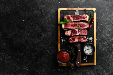 Steak on the bone on the kitchen board. Tomahawk steak on a black wooden background. Top view. Free space for copying.