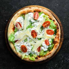 Homemade pizza: lettuce, tomatoes, cream and cheese. Takeaway food. Home delivery of food. On a black stone background.