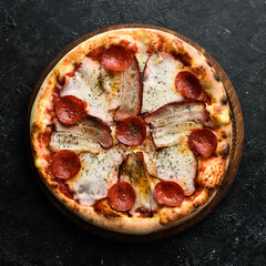 Traditional Italian pizza with bacon and pepperoni. Home delivery of food. On a black stone background.