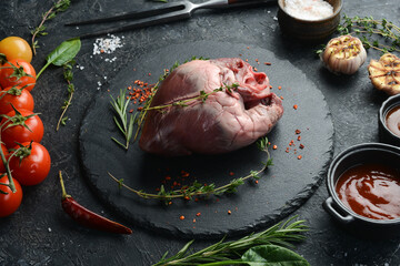 Raw pork heart is ready to cook with spices and herbs. Meat. On a black background.