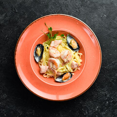 Seafood. Pasta with shrimp, mussels, cheese and basil in a plate. Italian dish. On a black stone background.