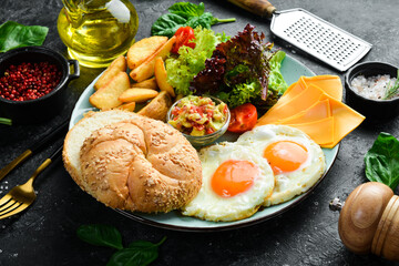 Breakfast. Scrambled eggs, bun, cheese, salad and sauce. On a black stone background.