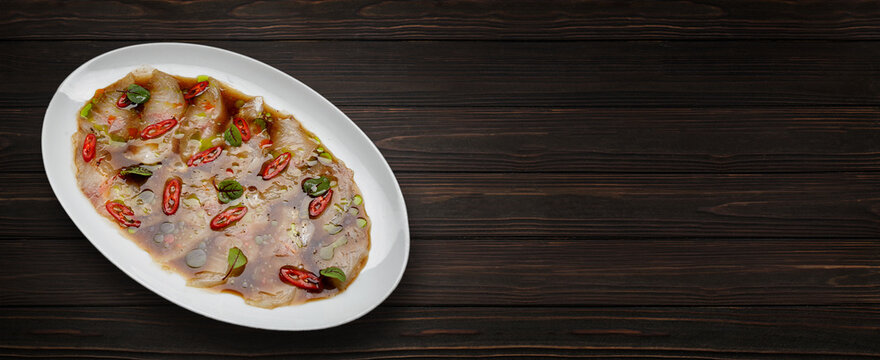 Dorado fish crudo in sauce with spices, on a wooden background