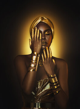 Artwork Portrait closeup Beauty fantasy african woman sexy face in gold paint. Golden metallic liquid skin hand creative design makeup. Fashion model girl posing shoot yellow light makeup artist