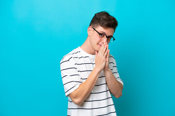 Young handsome Brazilian man isolated on blue background keeps palm together. Person asks for something