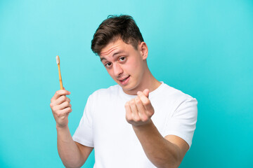 Young Brazilian man brushing teeth isolated on blue background making money gesture