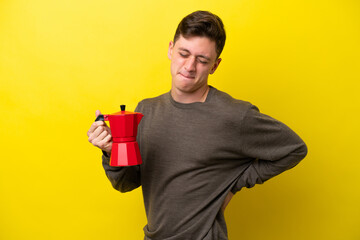 Young Brazilian man holding coffee pot isolated on yellow background suffering from backache for having made an effort