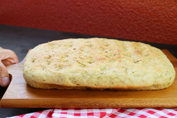 Hand Placing a Delectable Freshly Baked Herbed Focaccia Bread on the Table