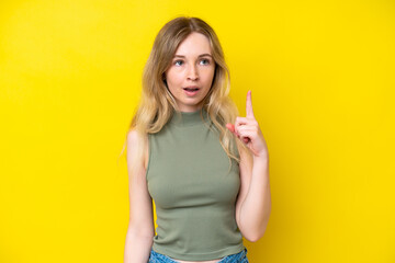 Blonde English young girl isolated on yellow background thinking an idea pointing the finger up