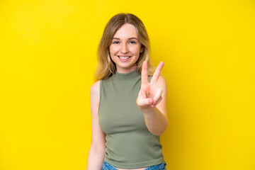 Blonde English young girl isolated on yellow background smiling and showing victory sign
