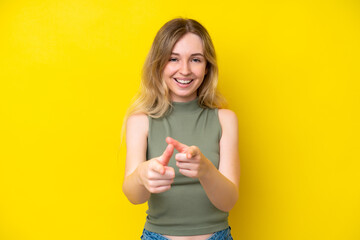 Blonde English young girl isolated on yellow background surprised and pointing front