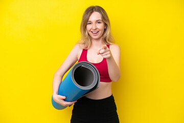 Young sport caucasian woman going to yoga classes while holding a mat isolated on yellow background surprised and pointing front